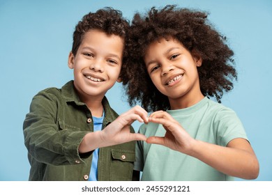 Happy African American children looking at camera, holding hands, showing heart gesture by hands, isolated on blue background. Concept of family, relationships, friendship - Powered by Shutterstock