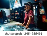 Happy African American concession stand worker in movie theater looking at camera.