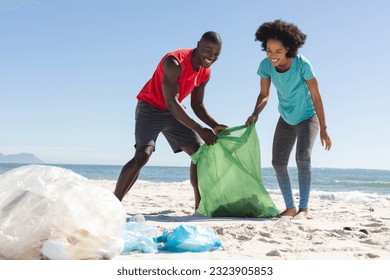 Happy african american couple cleaning sunny beach and collecting litter. Summer, lifestyle, free time, ecology, recycling and vacation, unaltered. - Powered by Shutterstock