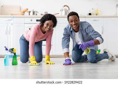 Happy African American Couple In Colorful Gloves Cleaning Floor Together In Kitchen, Using Cloth And Cleaning Sprays. Young Black Family House-keeping At Home And Having Fun, Copy Space