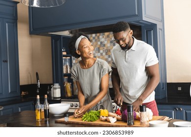 Happy african american couple cutting vegetables, preparing meal together in kitchen. Cooking, healthy lifestyle, togetherness, food and domestic life, unaltered. - Powered by Shutterstock