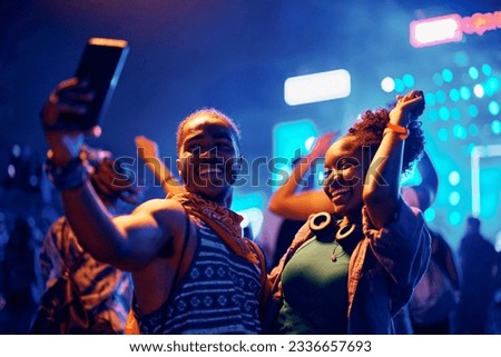 Happy African American couple dancing and taking selfie with cell phone during summer music festival. 