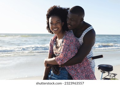 Happy african american couple embracing riding bike on sunny beach by the sea. Summer, romance, freedom, relaxation, togetherness and vacation, unaltered. - Powered by Shutterstock