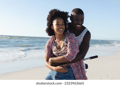 Happy african american couple embracing riding bike on sunny beach by the sea. Summer, romance, freedom, relaxation, togetherness and vacation, unaltered. - Powered by Shutterstock