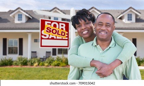 Happy African American Couple In Front Of Beautiful House And Sold For Sale Real Estate Sign.