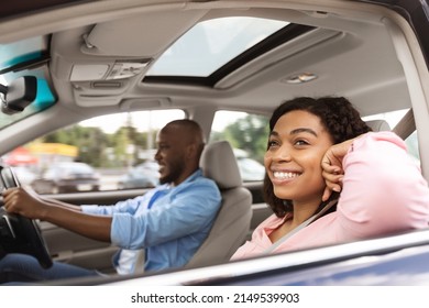 Happy African American Couple Going On Summer Vacation By Car. Beautiful Carefree Lady Sitting Inside Auto On Passenger Seat And Looking Out Open Window, Enjoying Safe Ride, Profile Side View