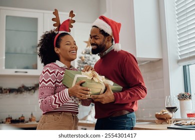 Happy African American couple having fun while exchanging Christmas gifts at home. - Powered by Shutterstock