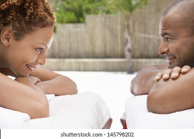 Happy African American couple lying face to face on massage tables at spa