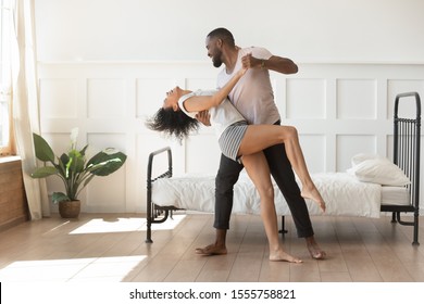 Happy african American couple in pajamas dance swaying in bedroom excited moving together, overjoyed smiling biracial husband and wife dancers have fun celebrate at home, relationships goal concept - Powered by Shutterstock