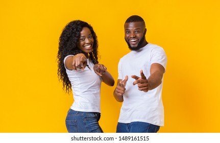 Happy African American Couple Pointing At Camera, yellow studio background, copy space