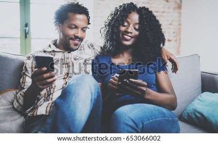 Happy african american couple relaxing together on the sofa.Young black man and his girlfriend using smartphones while rest at home in the living room. Horizontal,blurred background