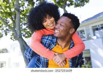 Happy african american couple riding piggyback in sunny garden, copy space. Outdoors, expression, love, togetherness and nature, unaltered. - Powered by Shutterstock