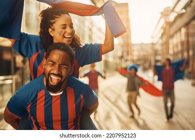 Happy African American Couple Of Soccer Fans Having Fun While Piggybacking On The Street. 