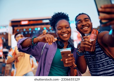 Happy African American couple taking selfie in front of music stage during summer festival. - Powered by Shutterstock