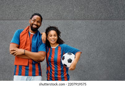 Happy African American couple wearing jerseys of their favorite soccer team and looking at camera. Copy space. 
