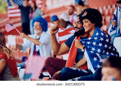 Happy African American couple wrapped in USA national flag watching sport match at the stadium. - Powered by Shutterstock