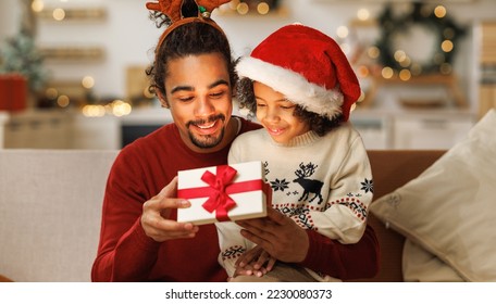 Happy African american curly boy with father opening christmas present, excited  kid  son with loving dad on couch. New Years traditions for families  - Powered by Shutterstock