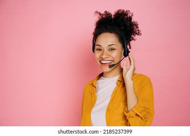 Happy african american curly haired young woman with headset, help desk worker, call center operator, consultant, talking with client, stand on isolated pink background, looks at camera,smile - Powered by Shutterstock