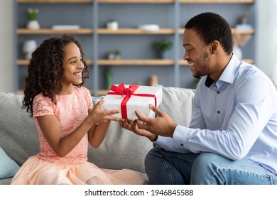 Happy African American Dad And Cute Daughter Celebrating Fathers Day At Home. Adorable Black Girl Greeting Her Smiling Young Father, Hugging Him And Giving Gift Box, Living Room Interior, Copy Space