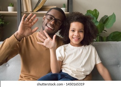 Happy African American Dad And Daughter Sit On Couch Wave Talking On Webcam Having Conversation, Smiling Black Father And Girl Child Blogger Say Hello To Viewers Record Vlog Or Blog