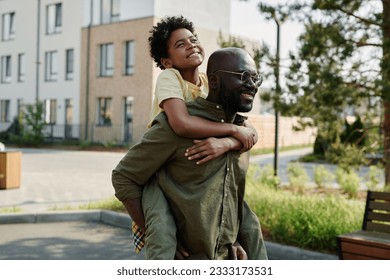Happy African American dad playing with his son outdoors during their walk