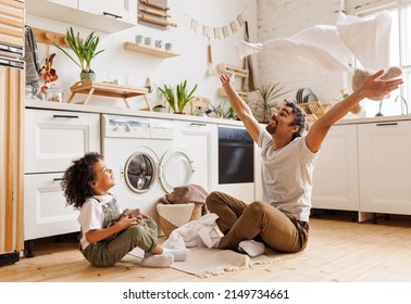 Happy african american dad and son smiling and tossing towels in air while sitting on floor near washing machine during household routine in kitchen at home - Powered by Shutterstock