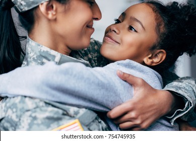 happy african american daughter hugging mother in military uniform at home