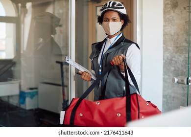 Happy African American Delivery Woman With Face Mask Carrying Thermal Bag While Making Food Delivery At Business Office.