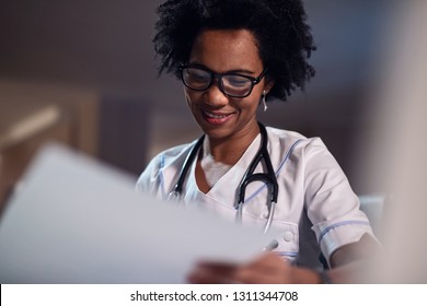 Happy African American Doctor Doing Paperwork And Reading Medical Files At Doctor's Office. 