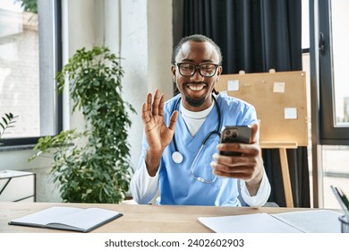 happy african american doctor with glasses waving at mobile phone camera and smiling joyfully - Powered by Shutterstock