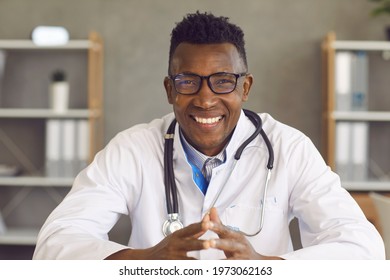 Happy African American Doctor Looking At Camera With Friendly Face Expression. Laptop Computer Screen Web Cam View Headshot Portrait Of Smiling Young Black Man In White Medical Lab Coat And Eyeglasses