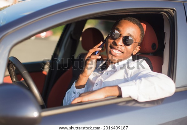 happy african american driving a car with a
phone, in the summer.