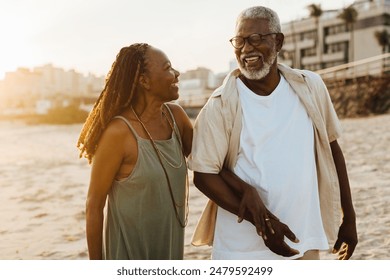 Happy African American elderly couple with braids walking on the beach at sunset, expressing love and joy. - Powered by Shutterstock