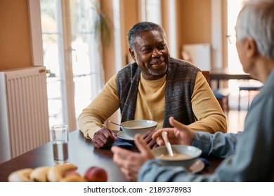 Happy African American elderly man and his friend communicating while eating lunch at dining table at nursing home.  - Powered by Shutterstock