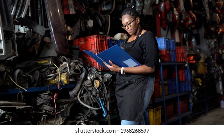 happy african american engineer warehouse worker checking list inventory of old used car engine in garage store. black woman  Inventory Manager in Recycle motor factory auto parts shop - Shutterstock ID 1968268597
