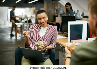 Happy African American entrepreneur communicating with her coworker while eating lunch on a break at work.  - Powered by Shutterstock