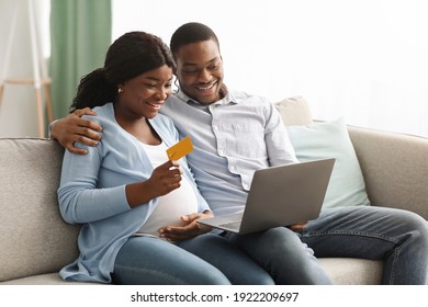 Happy African American Expecting Family Using Modern Laptop And Credit Card, Shopping Online At Home. Joyful Black Pregnant Woman Showing Her Smiling Husband New Website On Laptop, Copy Space