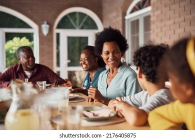 Happy African American Extended Family Gathering For Meal At Dining Table On Patio. Focus Is On Mother Talking To Her Kids. 