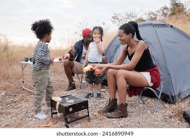 Happy African American family with adorable children enjoy weekend vacation camping outdoors in countryside, cheerful children laughing running around father holding apple fruit, bonding relationship - Powered by Shutterstock