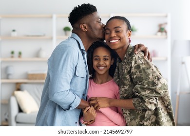 Happy african american family celebrating reunion with mom soldier, happy black man father kissing and hugging mother in military uniform and smiling, home interior, copy space - Powered by Shutterstock