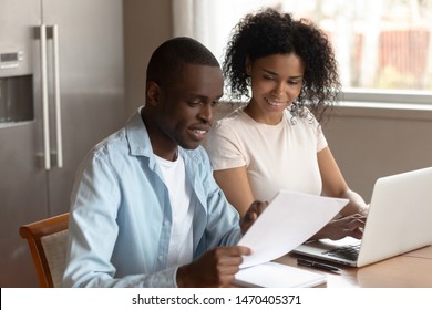 Happy African American Family Couple Sitting At Home With Laptop, Holding Paper Documents, Using Online Banking Application, Planning Family Budget, Monthly Expenses, Reviewing Taxes, Domestic Bills.