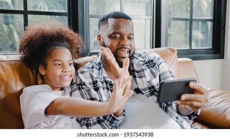 Happy African American Family Dad And Daughter Having Fun And Using Mobile Phone Video Call On Sofa At House. Self-isolation, Stay At Home, Social Distancing, Quarantine For Coronavirus Prevention.