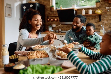 Happy African American family eating lunch together at dining table. Focus is on mother serving food. - Powered by Shutterstock