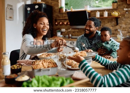 Happy African American family eating lunch together at dining table. Focus is on mother serving food.