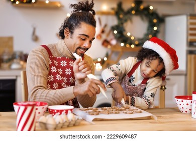 Happy african american family father and son in aprons making Christmas cookies together while cooking in kitchen at home, smiling boy helping dad to decorate xmas gingerbreads during winter holidays - Powered by Shutterstock