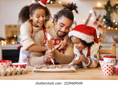 Happy african american family father and two kids in festive outfit making Christmas cookies together in kitchen at home during winter holidays, dad decorating xmas gingerbreads with small children   - Powered by Shutterstock