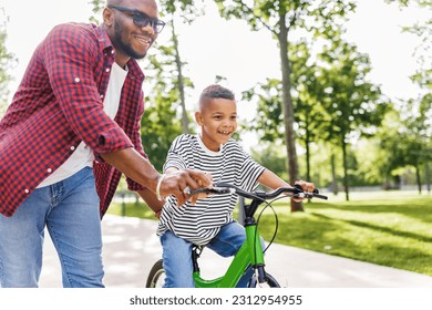 Happy african american family  father teaches boy son  to ride bike in  park   in nature - Shutterstock ID 2312954955