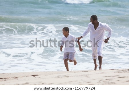 A happy African American family of father and son, man & boy child, running and having fun in the sand and waves of a sunny beach
