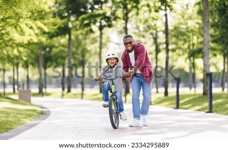 Happy african american family  father teaches boy son  to ride bike in  park   in nature

