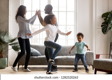 Happy African American Family And Funny Active Children Having Fun Dancing Together At New Home, Cheerful Black Parents And Two Kids Enjoying Moving To Music Spending Weekend Time In Living Room